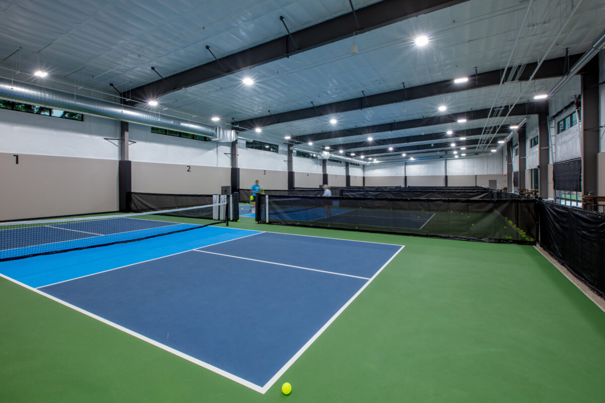 Indoor pickleball courts featuring bright green and blue and interior lights.
