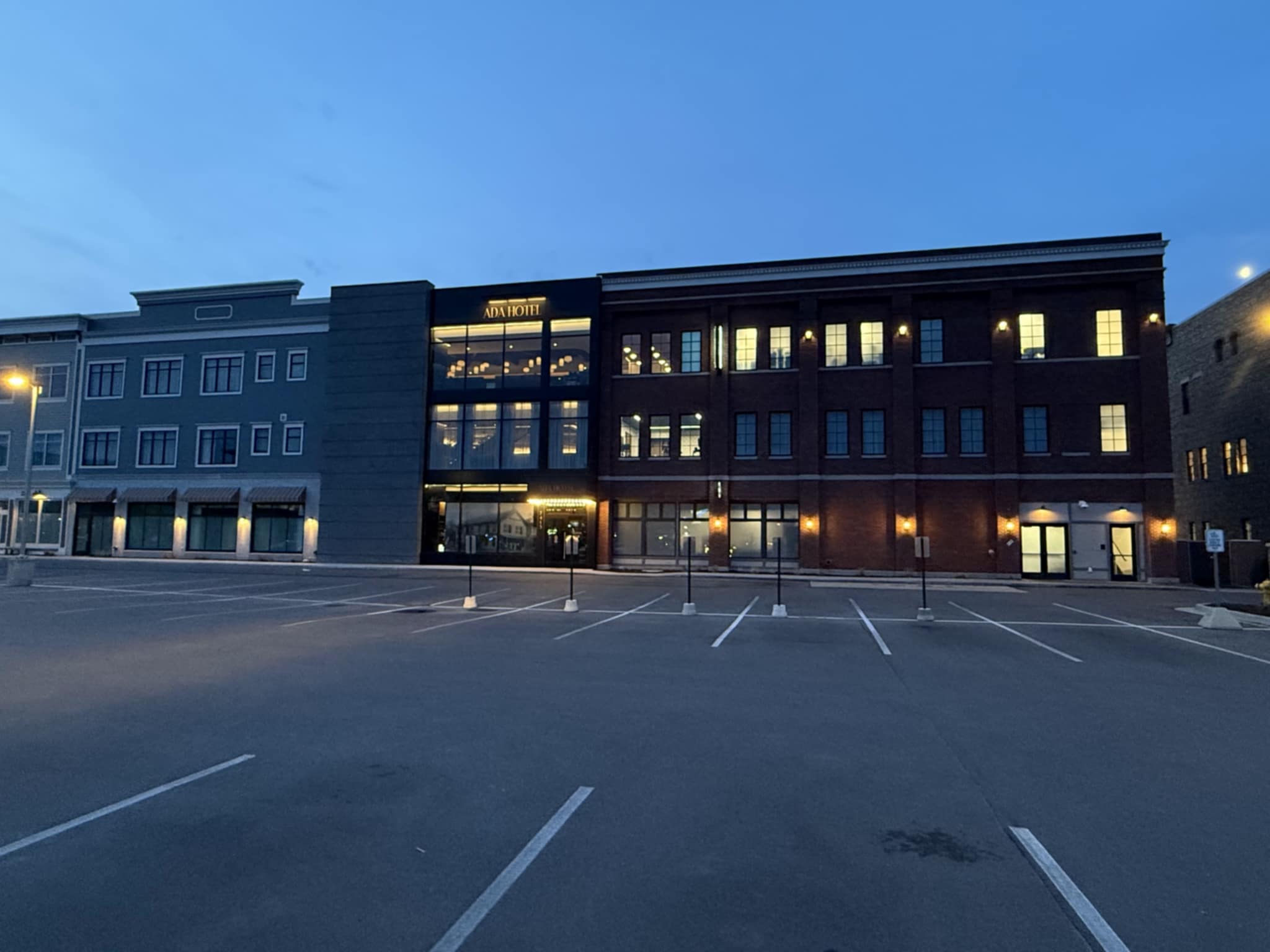 The outside of the Ada Hotel with parking lot, windows, at night
